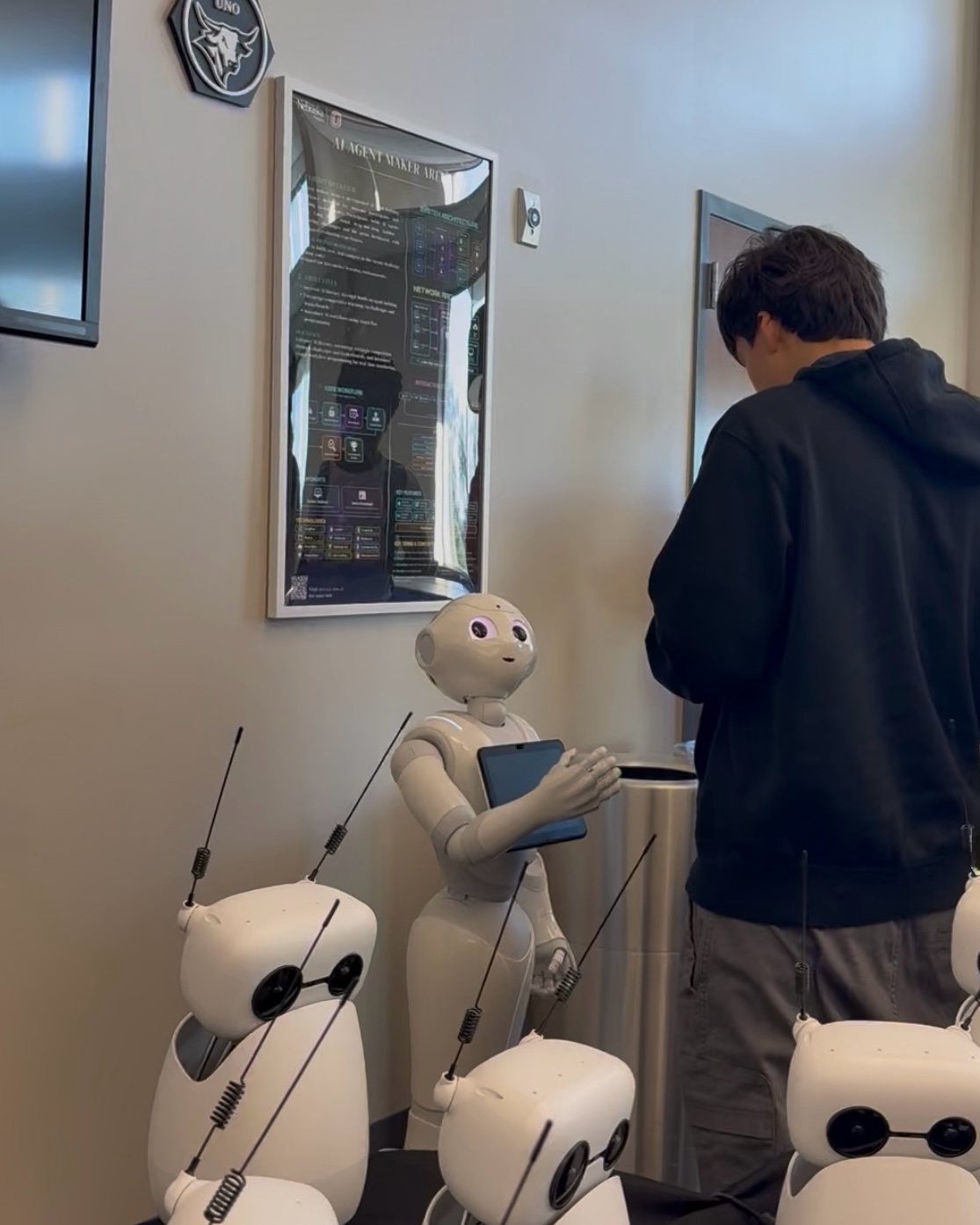 A Central High student stands in front of a humanoid robot near the AI Agent Maker Arena, with several smaller robots and the Maker Arena display visible nearby.